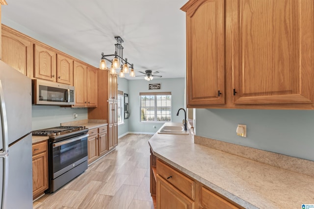 kitchen featuring a ceiling fan, a sink, appliances with stainless steel finishes, light countertops, and hanging light fixtures