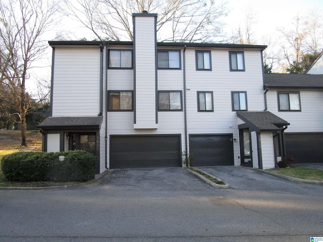 multi unit property with driveway, a chimney, and an attached garage