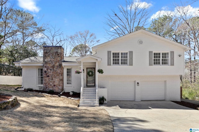 tri-level home with a garage, brick siding, driveway, and a chimney