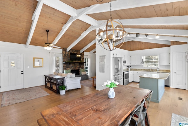 dining space with ceiling fan with notable chandelier, a stone fireplace, plenty of natural light, and light wood-style flooring