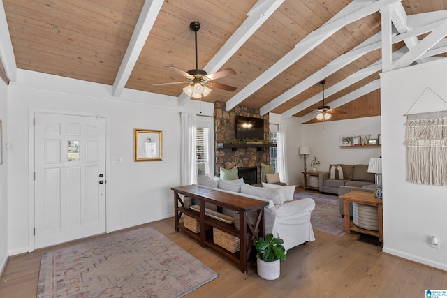 living room with lofted ceiling with beams, ceiling fan, a stone fireplace, light wood-style flooring, and baseboards