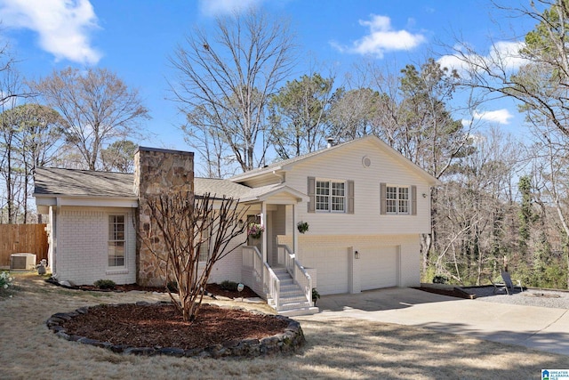 split level home with driveway, central AC unit, a chimney, an attached garage, and brick siding