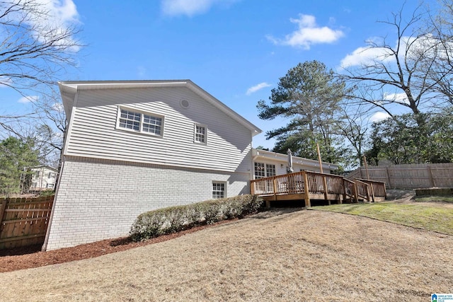 view of home's exterior with brick siding, fence, and a wooden deck