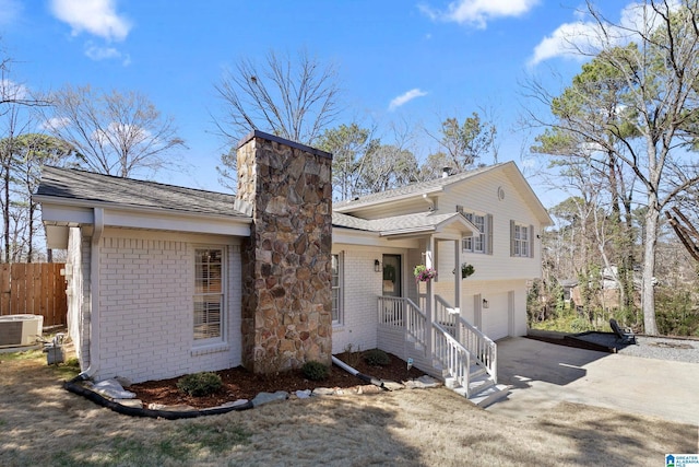 split level home with brick siding, a chimney, central AC unit, fence, and driveway