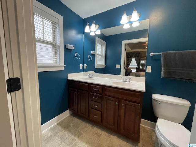 full bath featuring toilet, double vanity, baseboards, and a sink