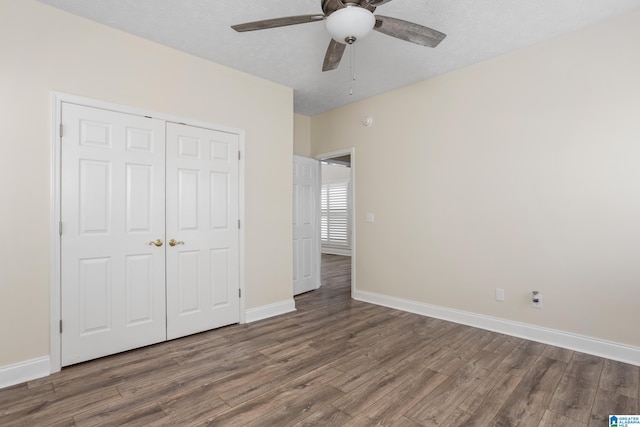 unfurnished bedroom featuring a closet, a textured ceiling, baseboards, and wood finished floors