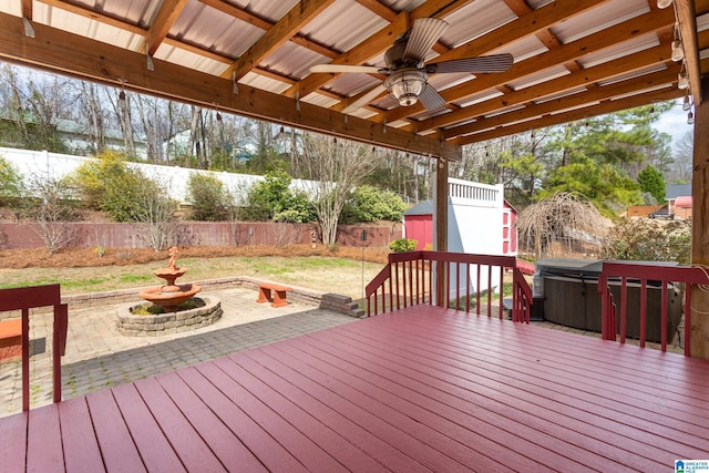 wooden terrace with a storage unit, a hot tub, a ceiling fan, a fenced backyard, and an outdoor structure