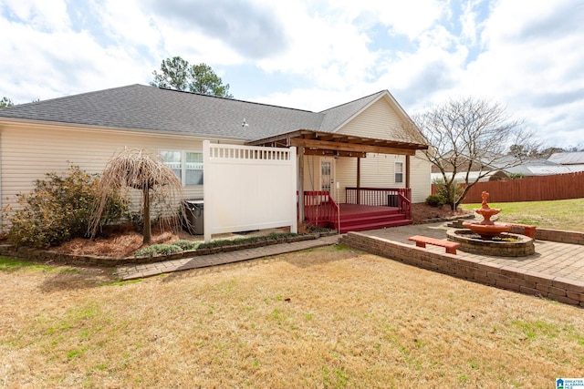 back of house featuring a yard, fence, and a shingled roof