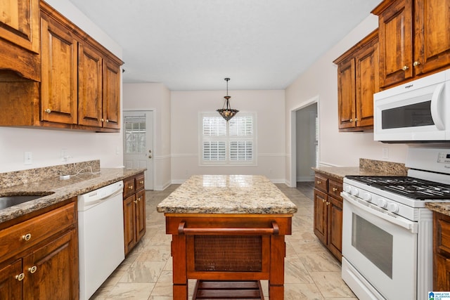 kitchen featuring light stone counters, a center island, brown cabinetry, white appliances, and baseboards