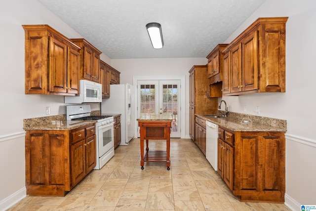 kitchen with light stone counters, french doors, brown cabinetry, a sink, and white appliances