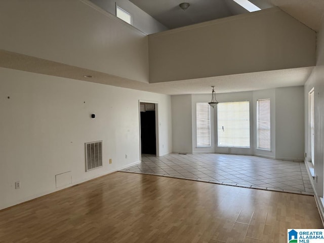 unfurnished room with baseboards, a high ceiling, visible vents, and light wood-style floors