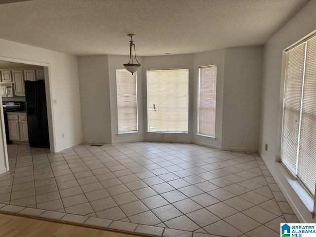 unfurnished dining area featuring light tile patterned flooring, a textured ceiling, and baseboards