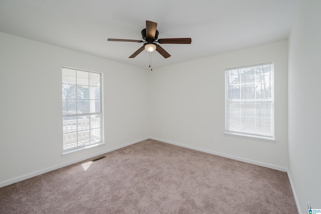 carpeted spare room featuring a ceiling fan, visible vents, and baseboards