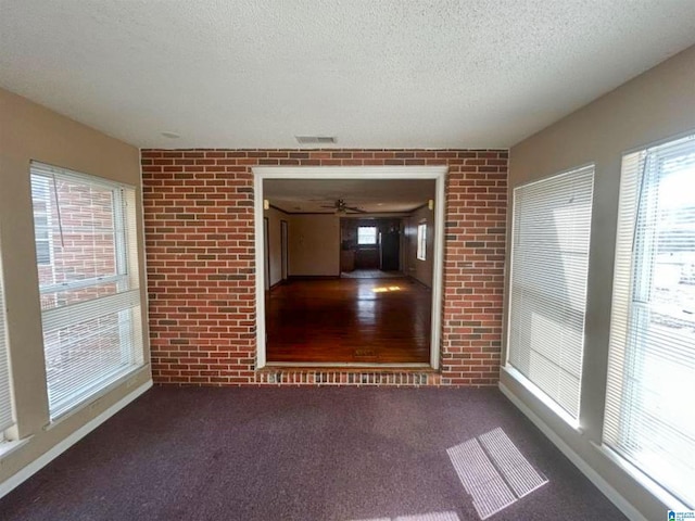 carpeted spare room with a textured ceiling, brick wall, visible vents, and a healthy amount of sunlight