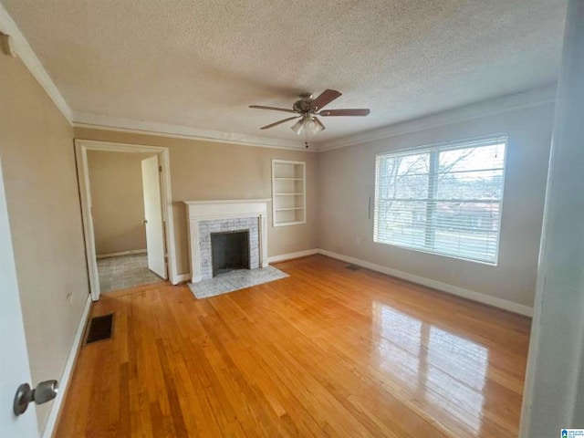 unfurnished living room featuring light wood-type flooring, a brick fireplace, visible vents, and crown molding