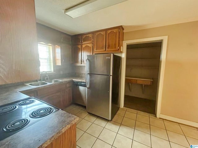 kitchen with light tile patterned floors, appliances with stainless steel finishes, brown cabinetry, and a sink