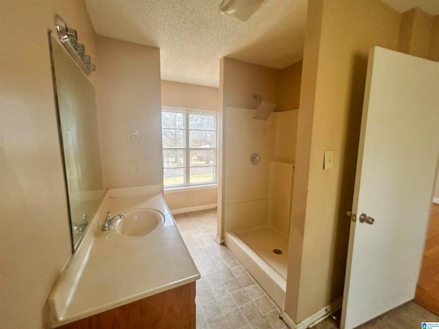 bathroom featuring a walk in shower, a textured ceiling, vanity, and baseboards