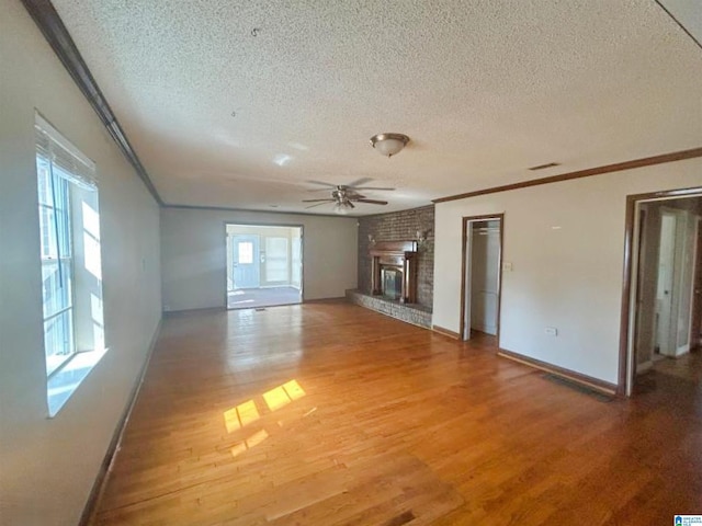 unfurnished living room featuring a ceiling fan, light wood-style flooring, ornamental molding, a textured ceiling, and a brick fireplace