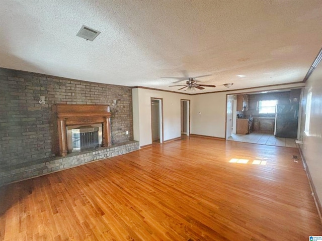 unfurnished living room with a textured ceiling, a fireplace, wood finished floors, visible vents, and crown molding