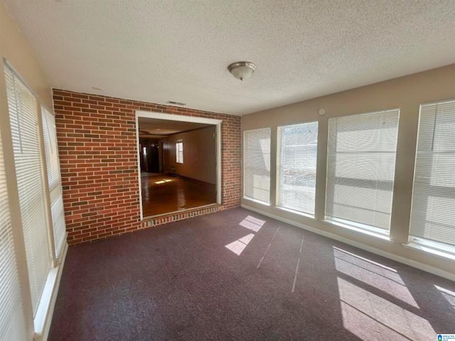 unfurnished room with brick wall, a healthy amount of sunlight, a textured ceiling, and carpet flooring