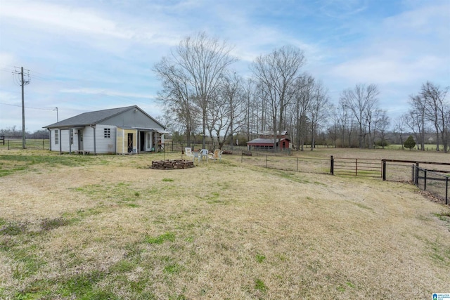 view of yard with an outdoor fire pit, a rural view, an outdoor structure, and fence