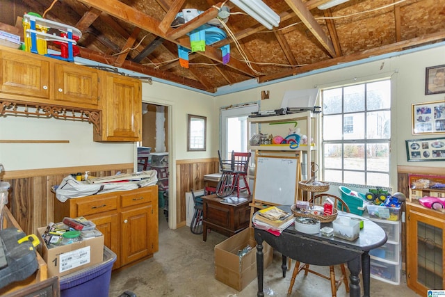 kitchen featuring brown cabinetry, concrete floors, wainscoting, and wood walls