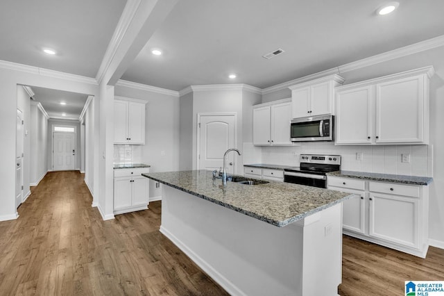 kitchen featuring visible vents, an island with sink, light stone counters, stainless steel appliances, and a sink