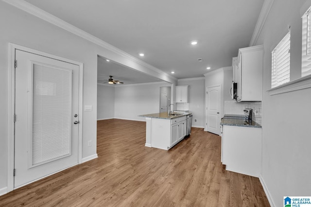 kitchen with white cabinets, appliances with stainless steel finishes, light wood-type flooring, tasteful backsplash, and dark stone countertops