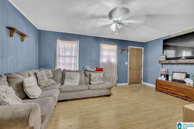 living area featuring a ceiling fan, a textured ceiling, baseboards, and wood finished floors