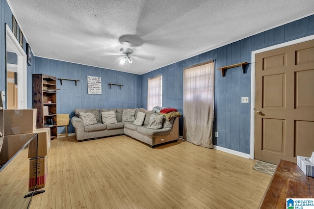 living room with baseboards, ceiling fan, light wood-style flooring, and a textured ceiling