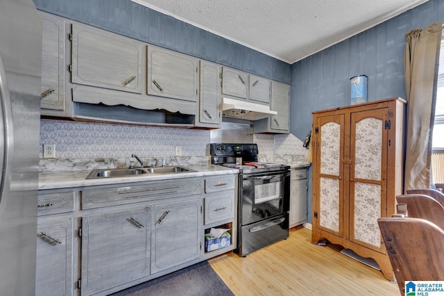 kitchen with a sink, under cabinet range hood, light countertops, and black range with electric stovetop