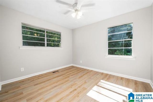 empty room featuring a healthy amount of sunlight, baseboards, visible vents, and wood finished floors