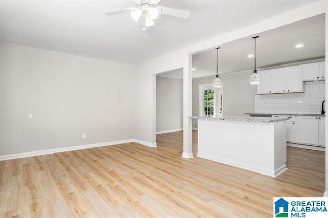 kitchen with light wood finished floors, baseboards, white cabinetry, and backsplash