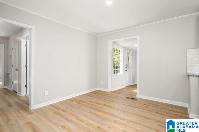 empty room with ornamental molding, visible vents, light wood-style floors, and baseboards