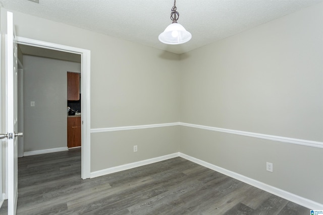 spare room featuring dark wood-style flooring, a textured ceiling, and baseboards