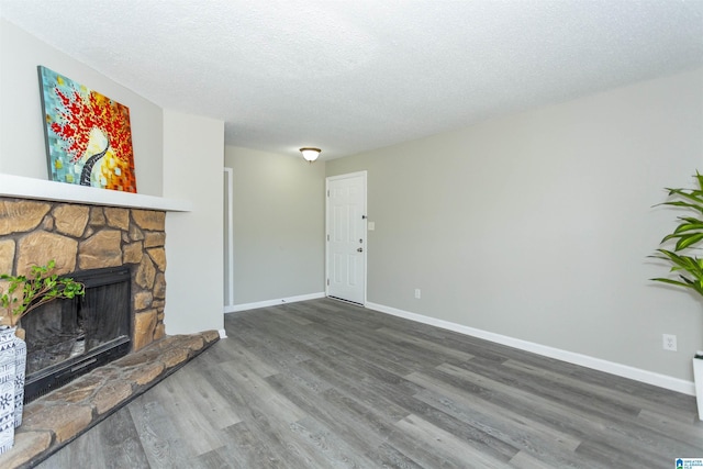 unfurnished living room featuring a textured ceiling, a stone fireplace, wood finished floors, and baseboards