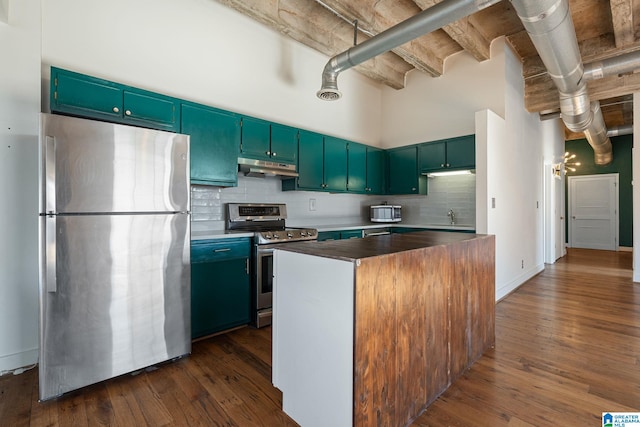 kitchen with decorative backsplash, a high ceiling, appliances with stainless steel finishes, dark wood-type flooring, and under cabinet range hood