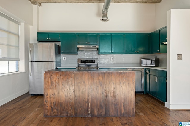 kitchen with under cabinet range hood, appliances with stainless steel finishes, backsplash, a center island, and dark wood finished floors