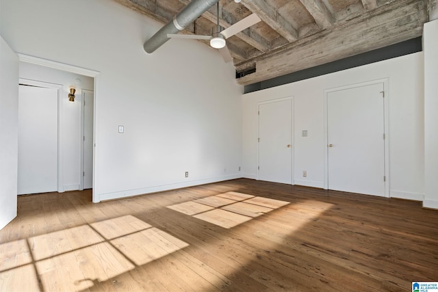 unfurnished bedroom with baseboards, hardwood / wood-style flooring, a towering ceiling, and a ceiling fan