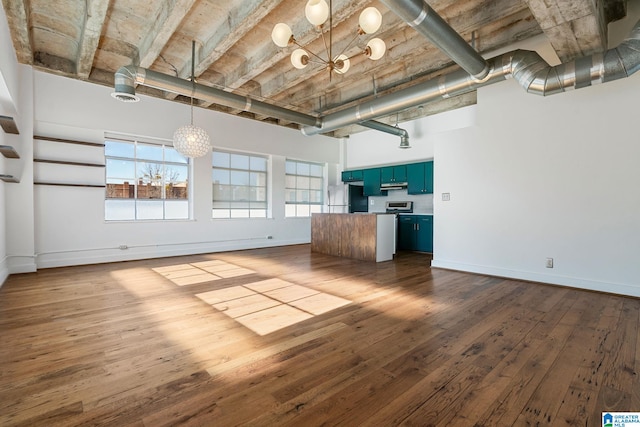 unfurnished living room with baseboards, dark wood-style floors, a baseboard radiator, a high ceiling, and a notable chandelier