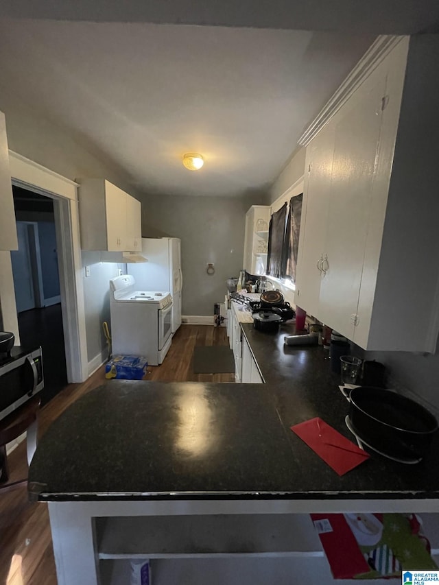 kitchen featuring dark wood-type flooring, white cabinets, range, stainless steel microwave, and dark countertops