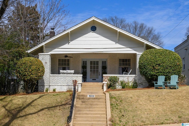 bungalow-style house with brick siding, a porch, a front lawn, and a ceiling fan