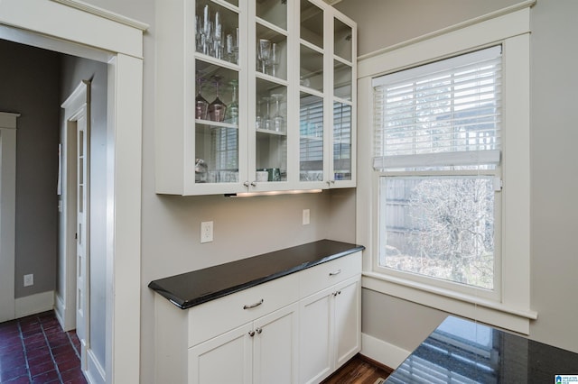 kitchen featuring white cabinetry, dark countertops, glass insert cabinets, and baseboards