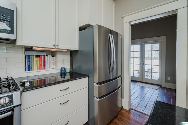 kitchen with dark stone countertops, stainless steel appliances, decorative backsplash, and white cabinetry