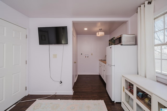 kitchen featuring stainless steel microwave, white cabinetry, freestanding refrigerator, baseboards, and dark wood-style flooring