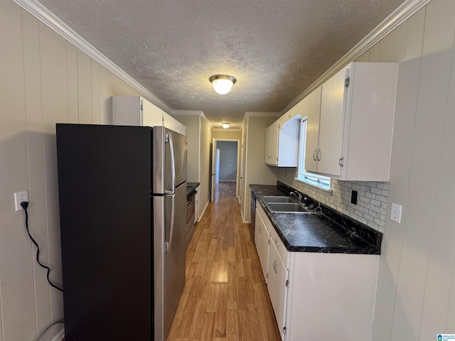 kitchen featuring a sink, freestanding refrigerator, light wood finished floors, dark countertops, and crown molding