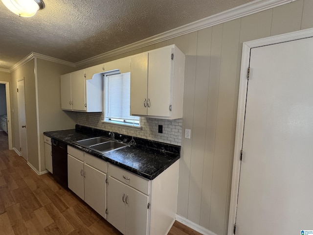 kitchen featuring wood finished floors, a sink, ornamental molding, dishwasher, and dark countertops