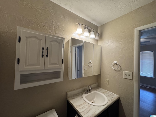 bathroom featuring a textured ceiling, a textured wall, and vanity