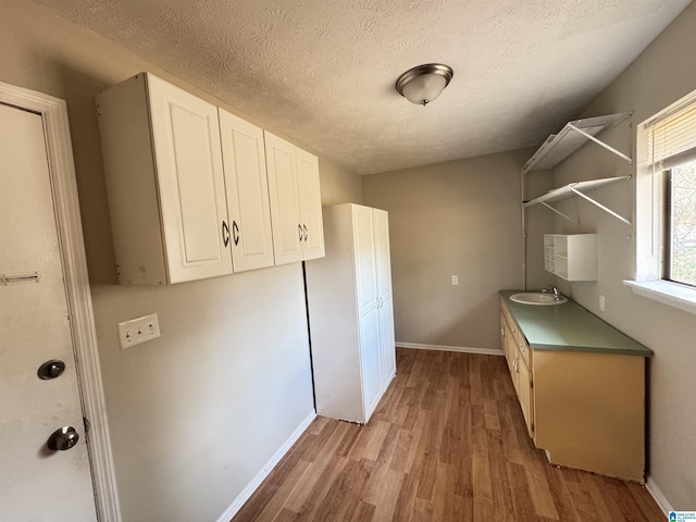 laundry room with a textured ceiling, a sink, light wood-style flooring, and baseboards