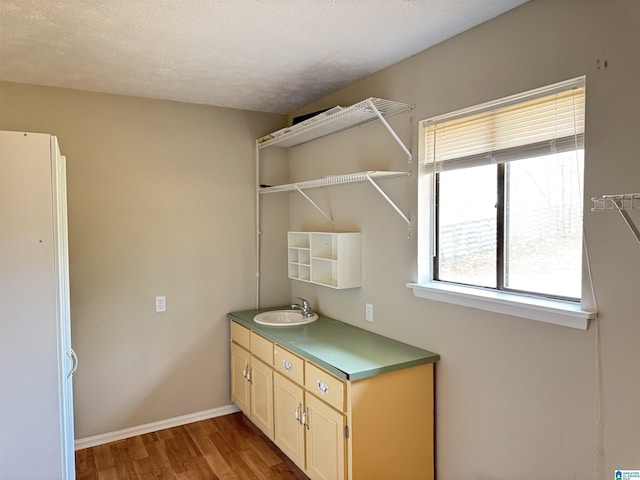 clothes washing area featuring a textured ceiling, baseboards, a sink, and wood finished floors